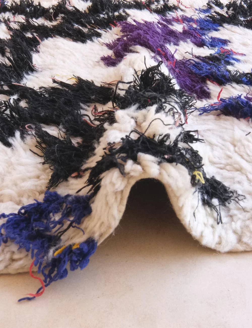 Close-up of a textured fabric with black, white, and purple colors on a beige background.