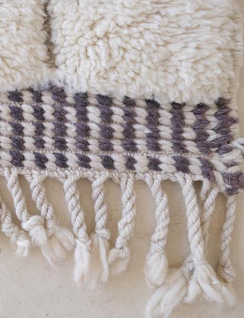 Close-up of Moroccan Beni Mrirt wool rug with thick white pile, black and white woven border, and twisted fringed tassels.