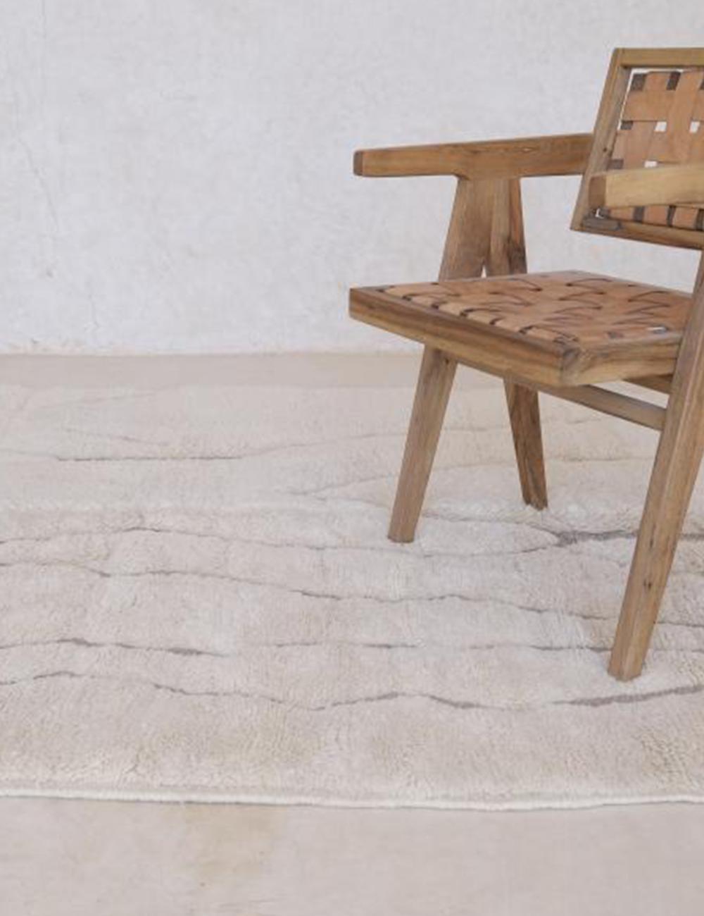 Contemporary Moroccan Beni Mrirt wool rug in beige with subtle irregular gray lines, styled with a wooden chair.