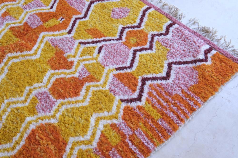 Close-up of modern Moroccan Boujad wool rug with vibrant yellow, orange, and pink zigzag geometric patterns and fringed edge.