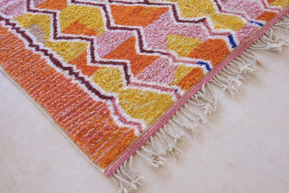 Modern Moroccan Boujad wool rug with vibrant orange, pink, and yellow geometric zigzag patterns and white fringed edges.