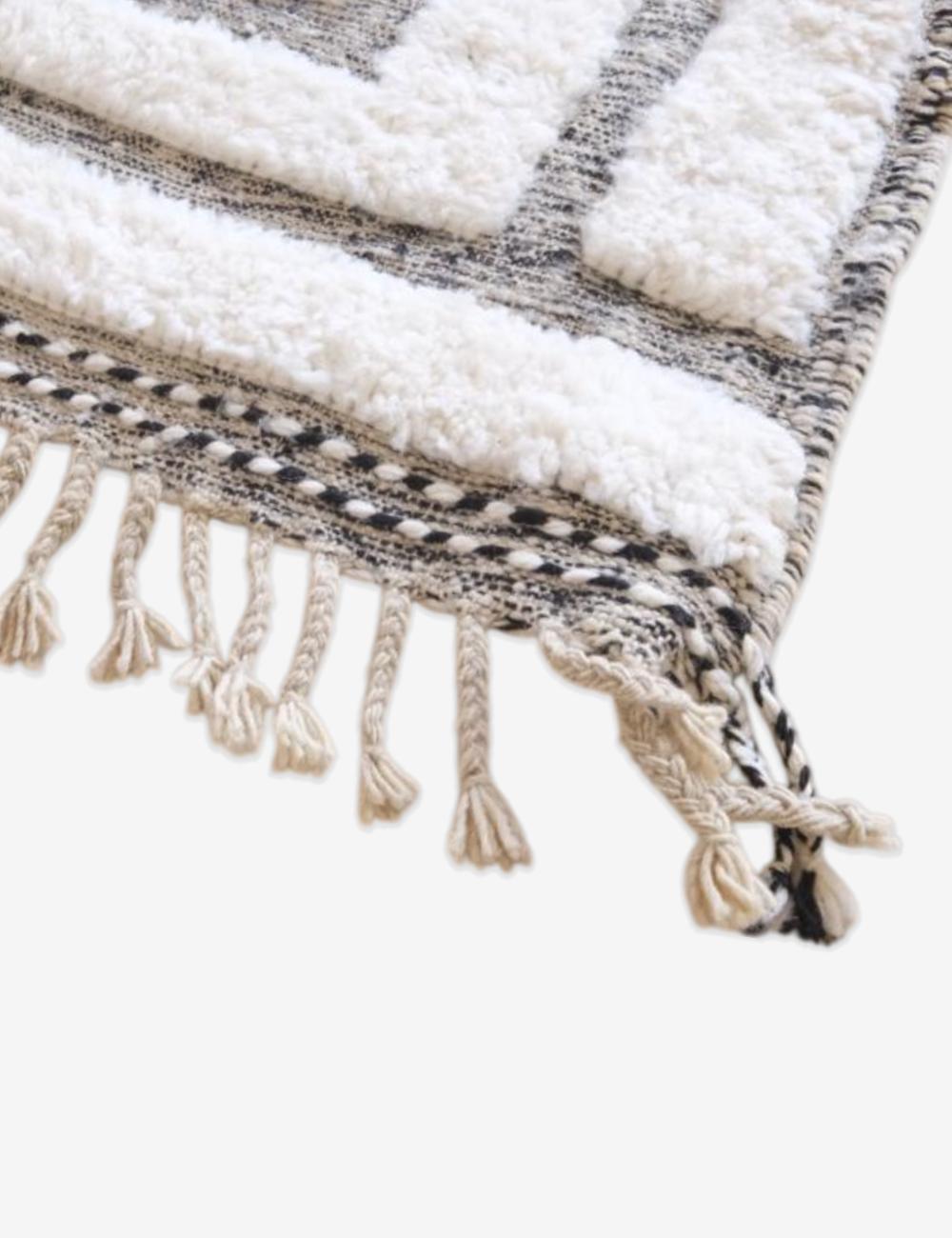 Close-up of Moroccan Beni Ourain wool rug with black geometric pattern and decorative fringed tassels