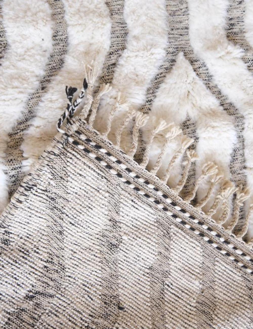Front and back view of Moroccan Beni Ourain wool rug showing black geometric stripes, fringed tassels, and woven underside.
