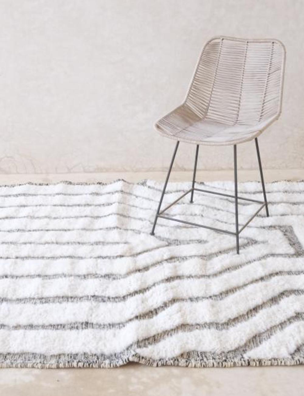 Moroccan Beni Ourain wool rug with black horizontal stripes styled in a modern interior with a wooden chair.