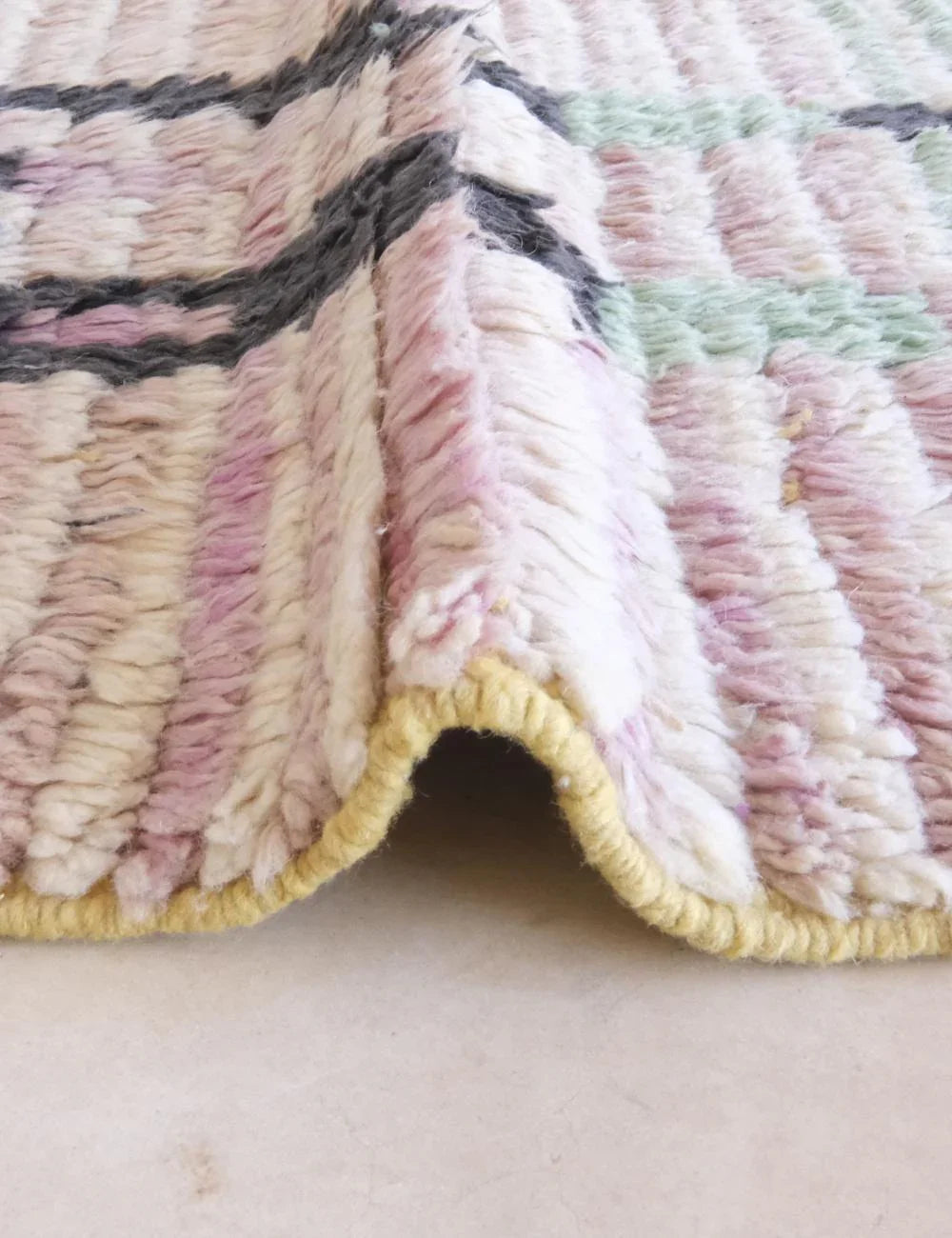 Close-up of a textured, multicolored rug with a yellow border on a light background.