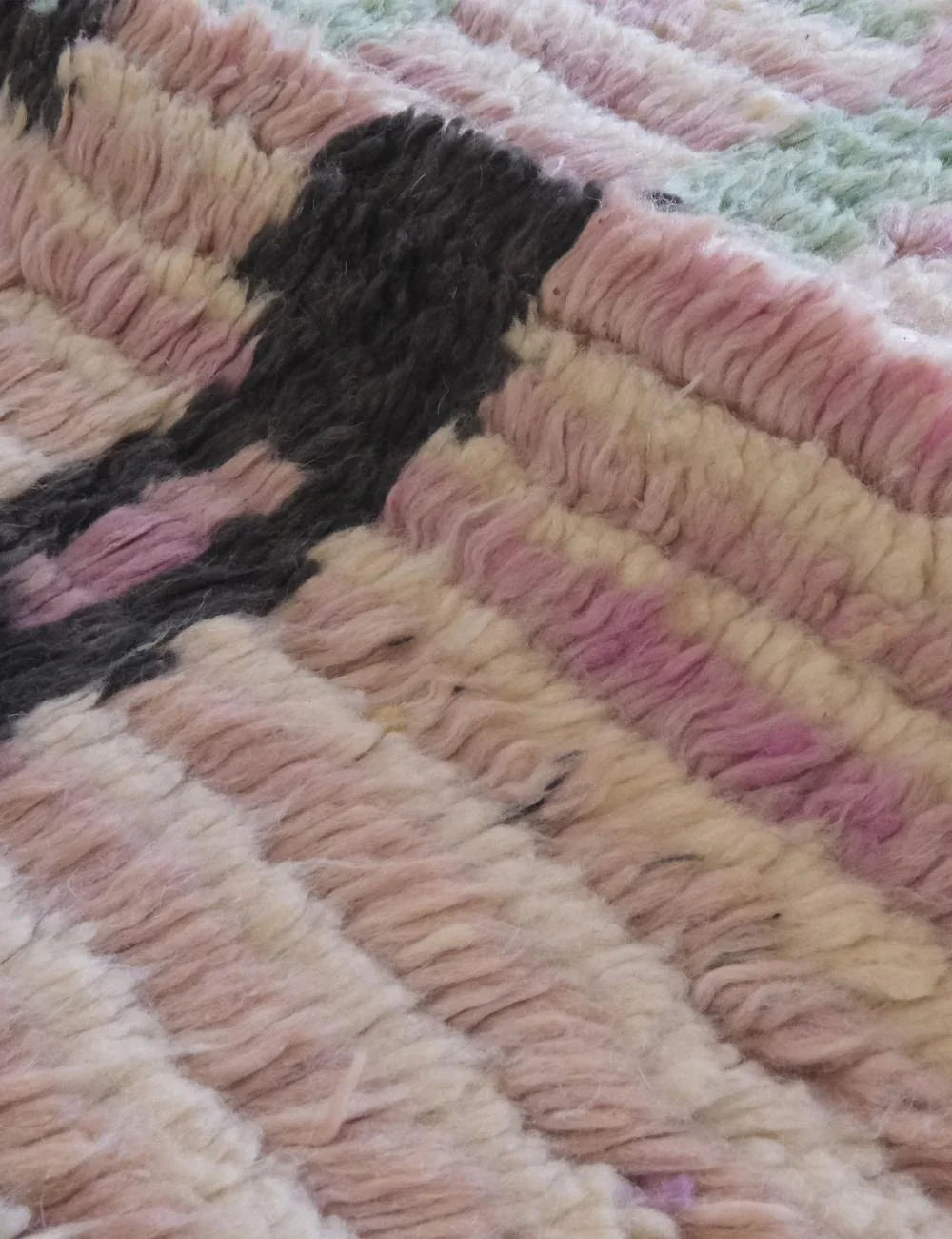 Close-up of a textured rug with pink, black, and beige colors.
