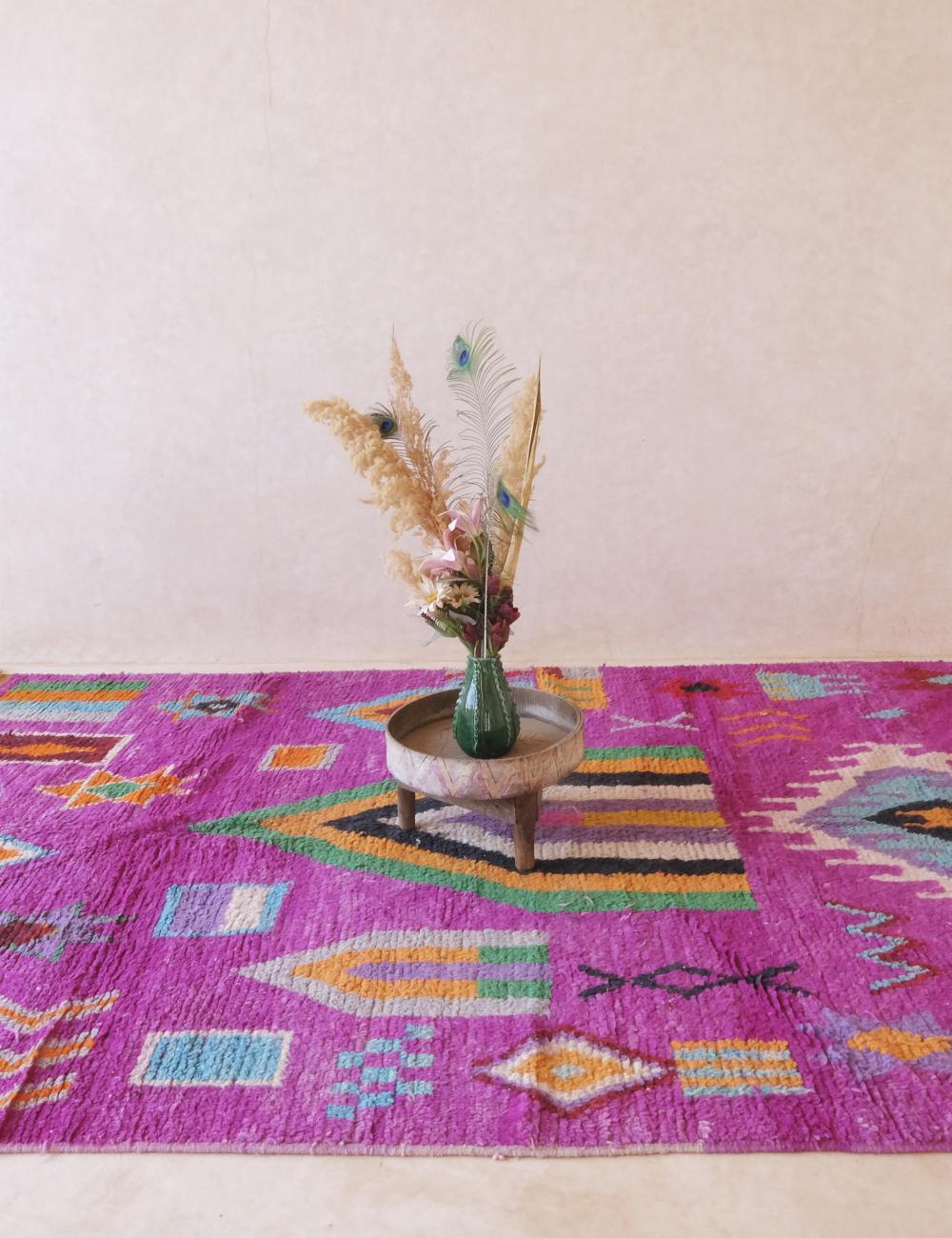 Colorful patterned rug with a vase and flowers on a wooden table against a white wall.