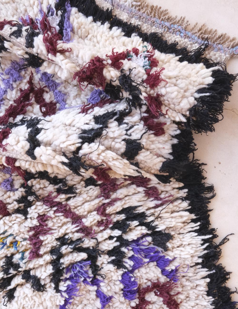 Close-up of a textured fabric with a geometric pattern in black, white, purple, and red.