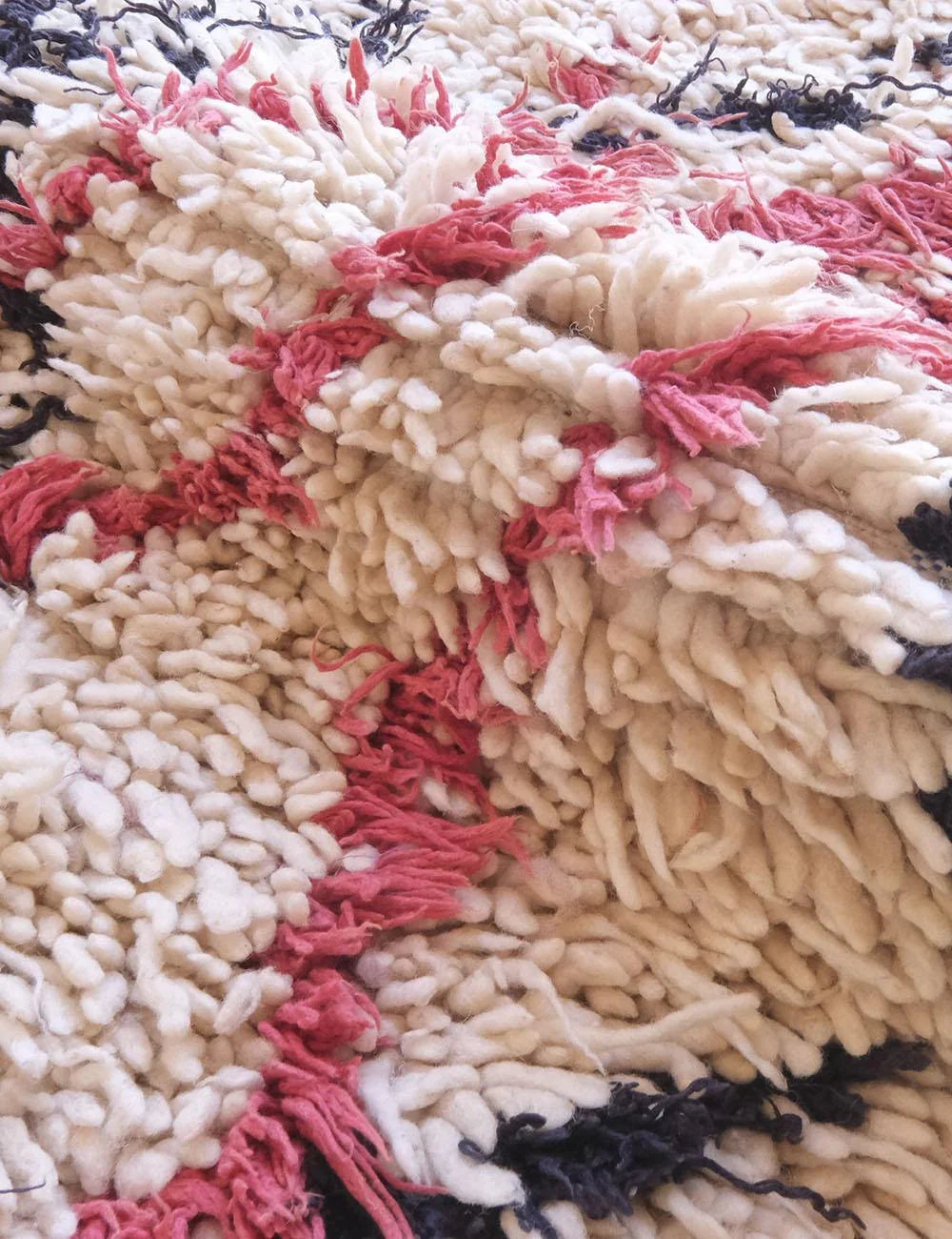 Close-up of a textured rug with red, white, and black patterns.