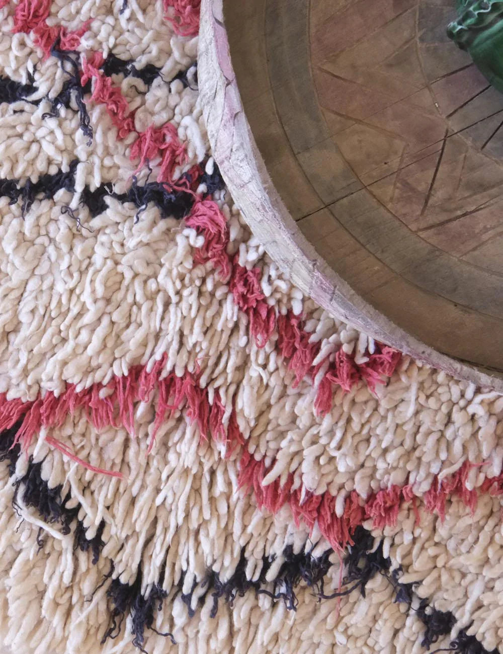 Close-up of a textured rug with pink and black patterns on a wooden floor.