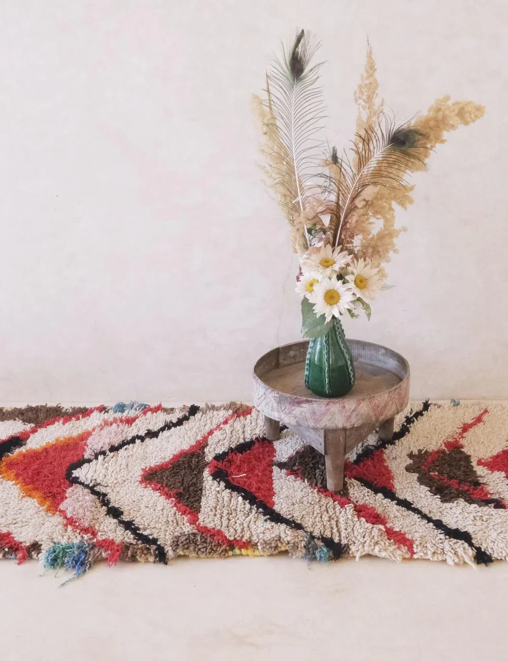 Decorative rug with geometric pattern, wooden table with vase of flowers, and white wall background