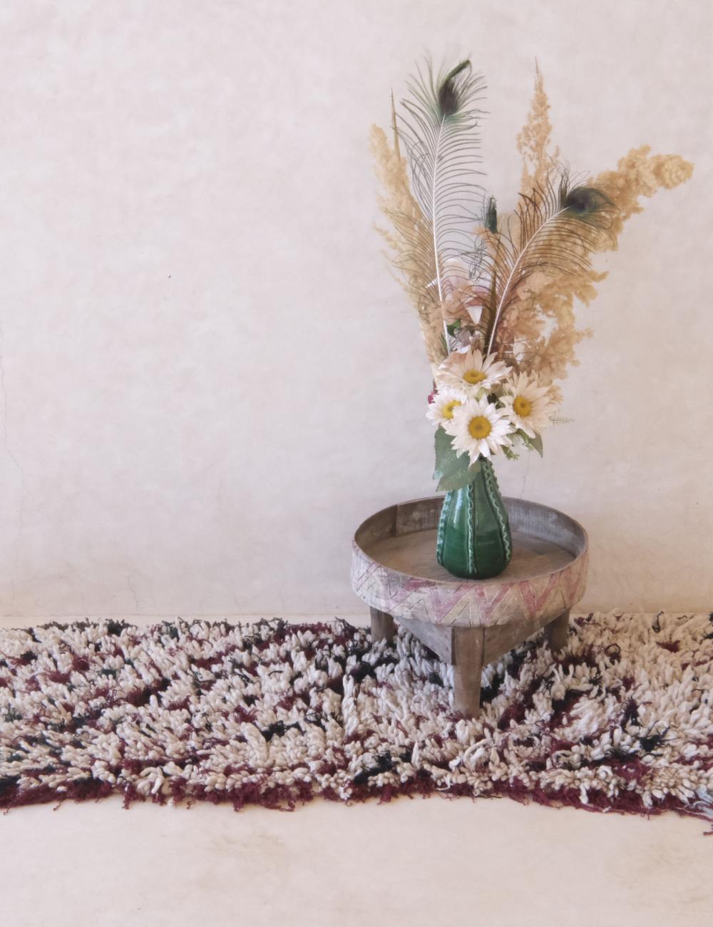 Vase with flowers and greenery on a small round table against a plain wall.