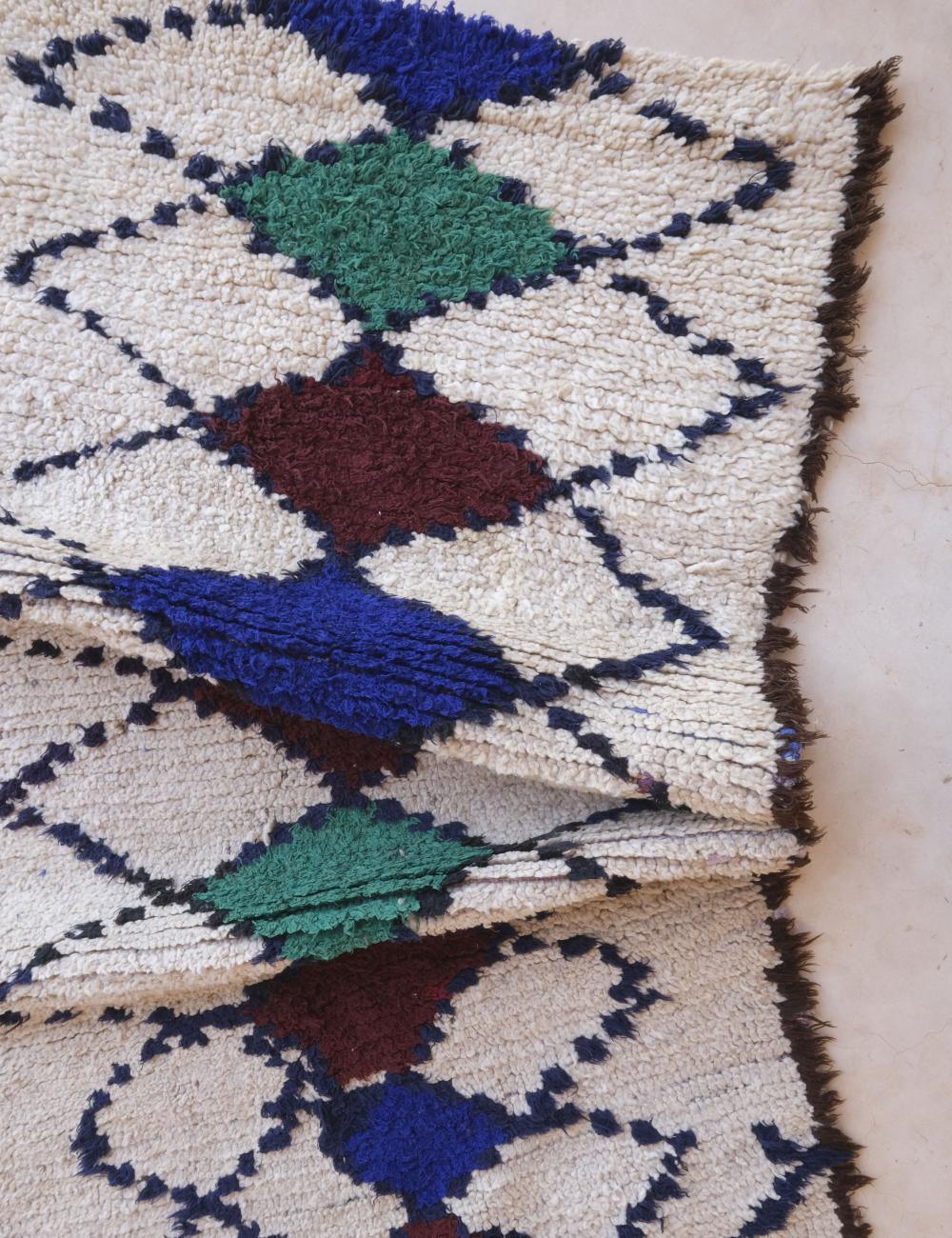 Close-up of a geometric patterned rug with blue, green, and brown colors on a beige background.