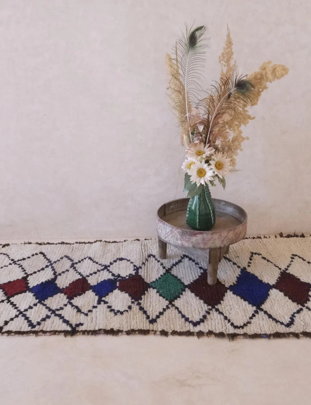 Decorative vase with flowers on a small table against a neutral wall, placed on a patterned rug.