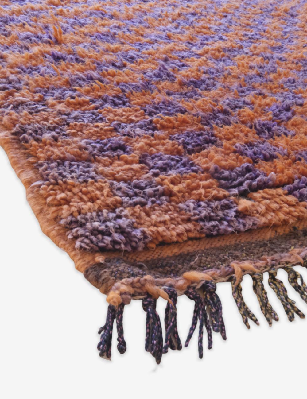 Close-up of a textured rug with orange and purple pattern on a white background