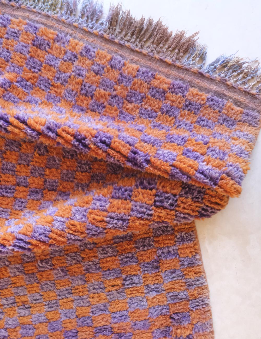 Close-up of a checkered blanket with orange and purple pattern on a white background