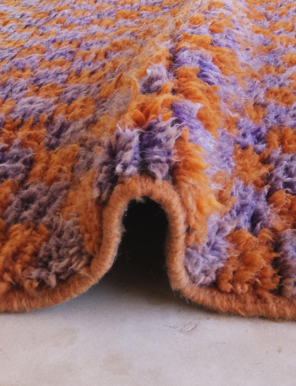 Close-up of a textured orange and purple rug corner on a light background