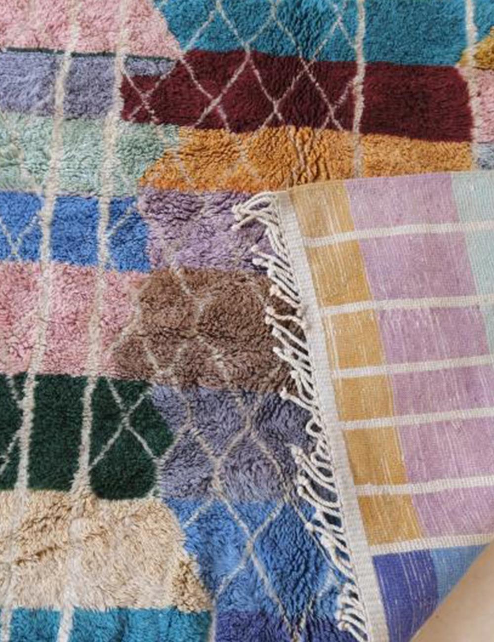 Contemporary Moroccan Beni Mrirt wool rug with multicolor geometric squares and white lattice pattern, folded corner showing striped backside with fringes.