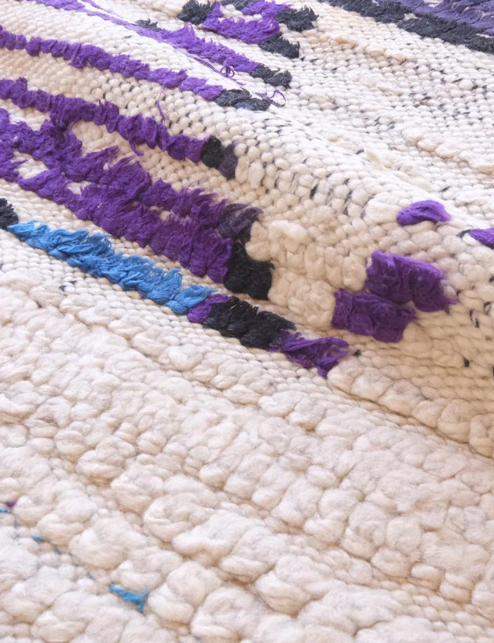 Close-up of a textured fabric with purple, black, and blue patterns on a beige background