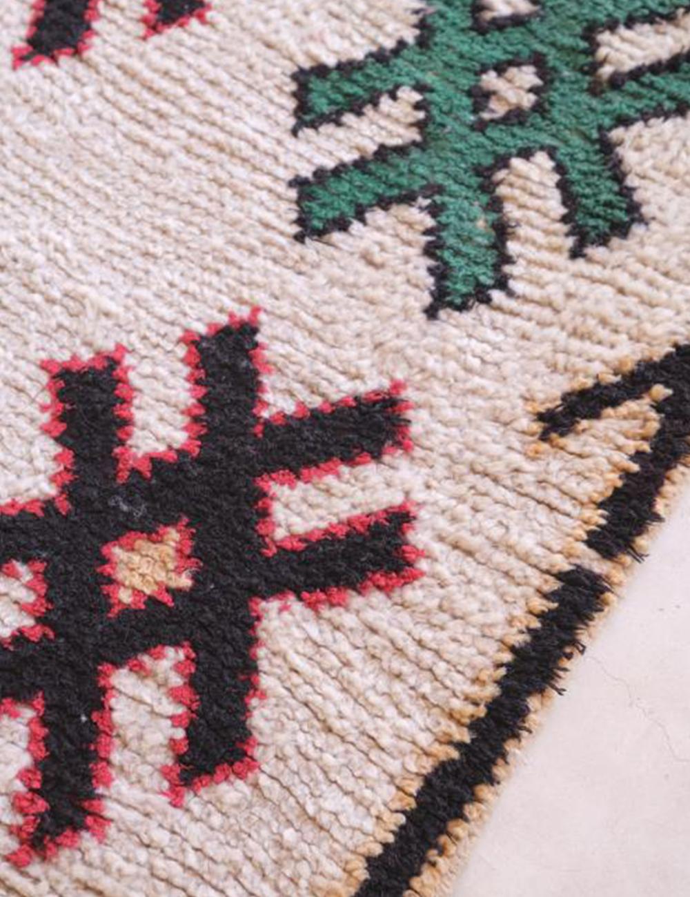 Close-up of a textured fabric with geometric patterns in black, red, and green on a beige background.