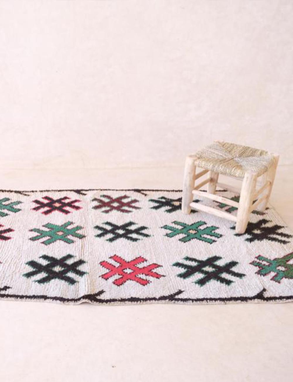 Decorative rug with hashtag pattern on a white floor, featuring a small stool.