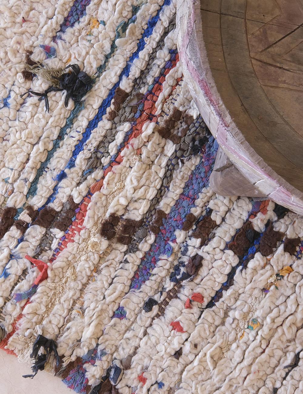 Close-up of a textured rug with multicolored patterns and a wooden object on top.