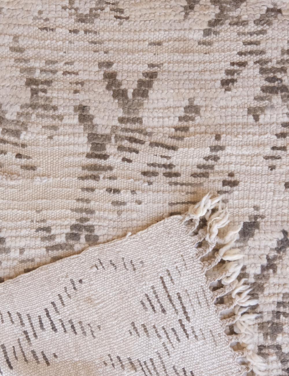 Close-up of a textured beige and brown rug with a fringed edge.