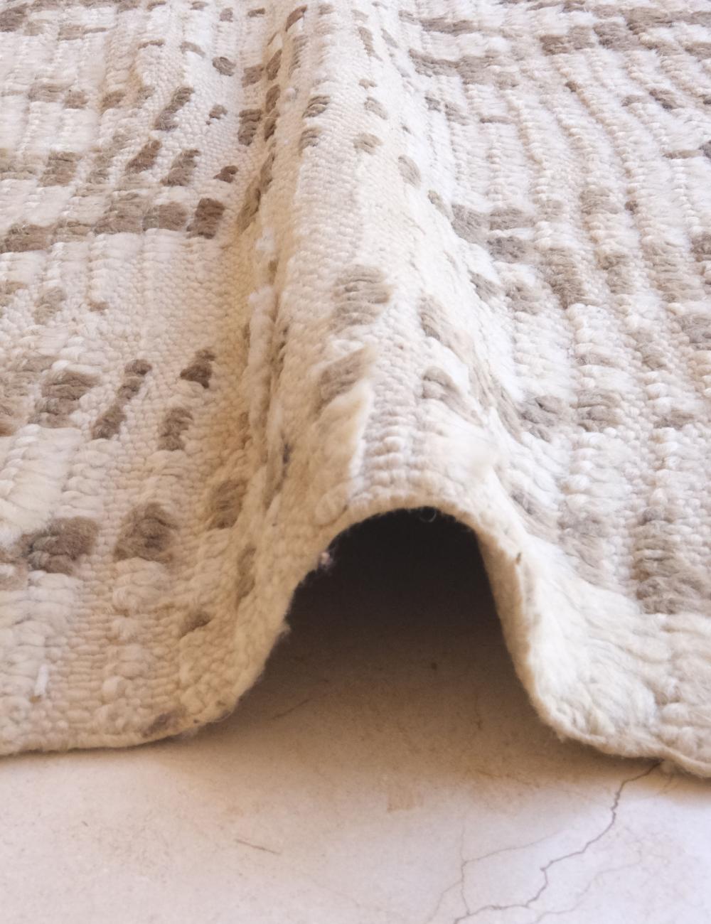 Close-up of a textured beige rug on a light-colored floor.