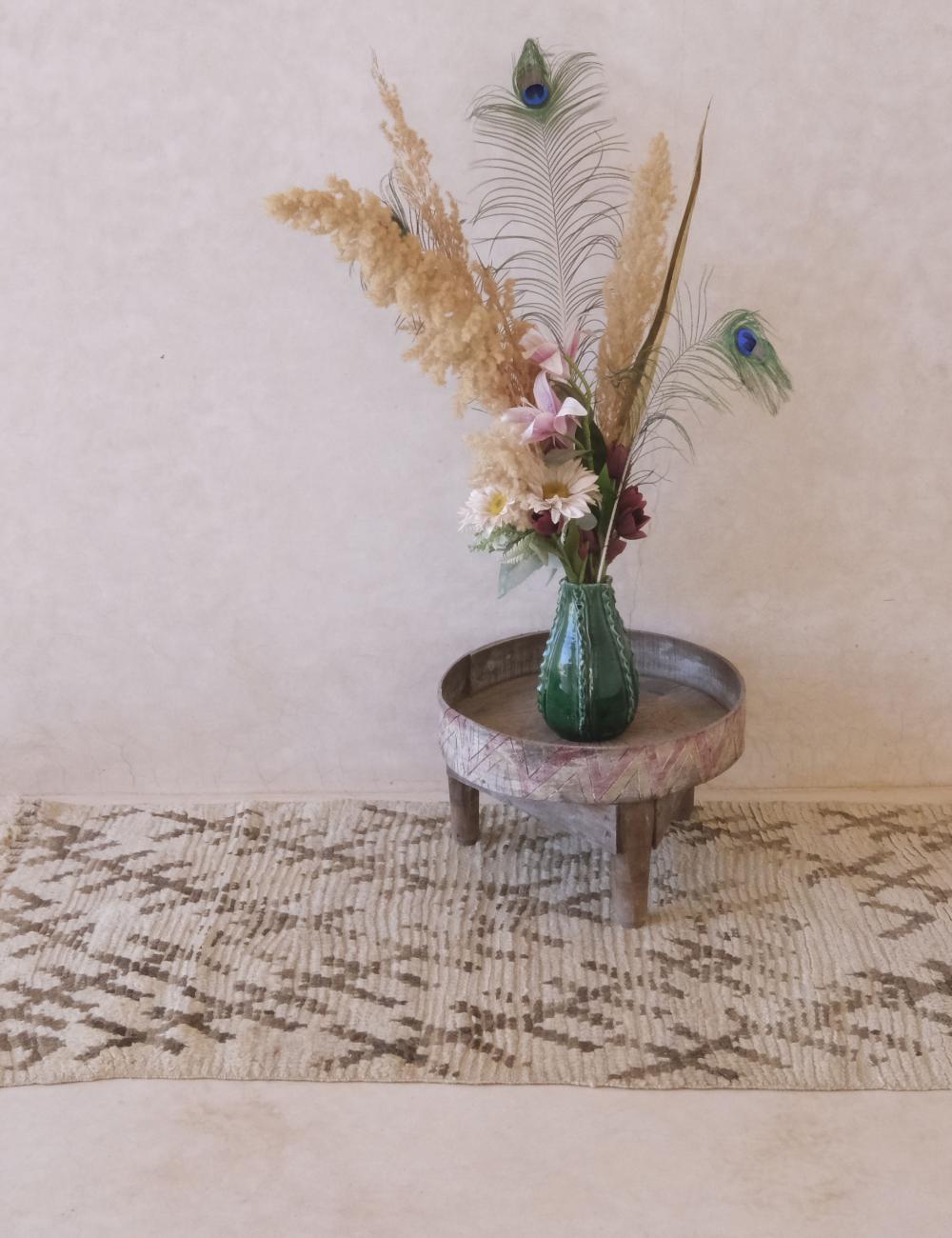 Decorative vase with flowers and peacock feathers on a small round table against a plain wall.