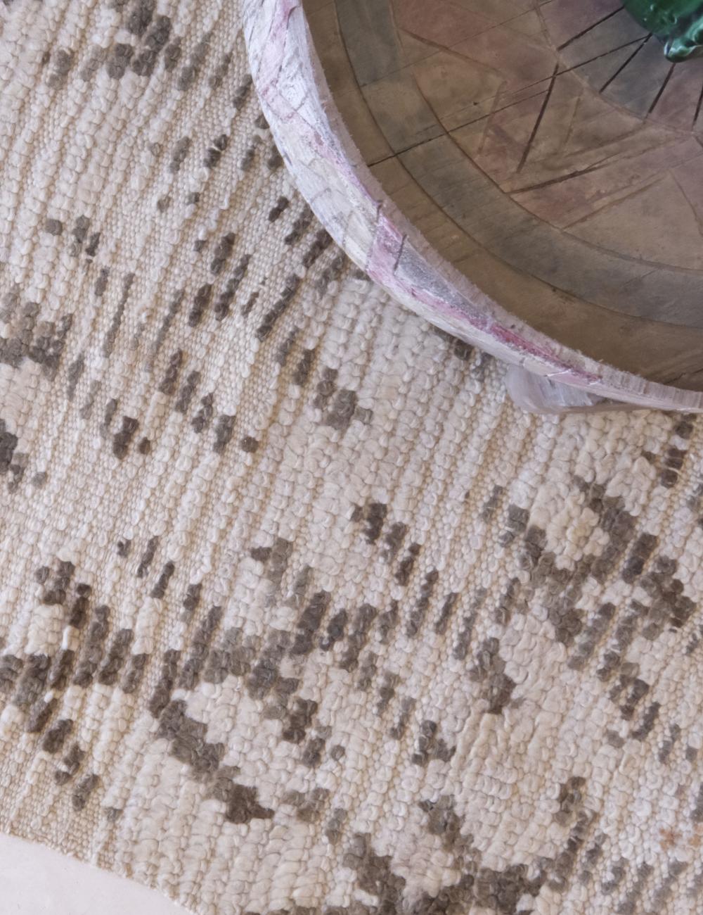 Close-up of a textured rug with a wooden chair leg in the corner.