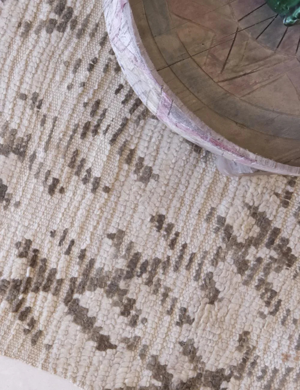 Close-up of a textured rug with a wooden chair leg in the corner.