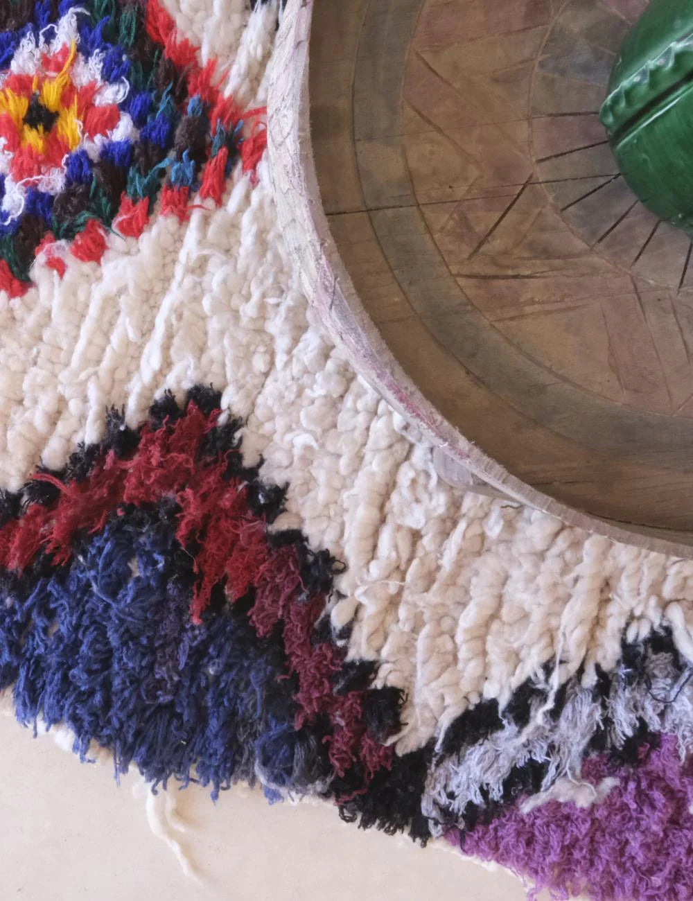 Close-up of a textured rug with colorful patterns and a wooden object on top.