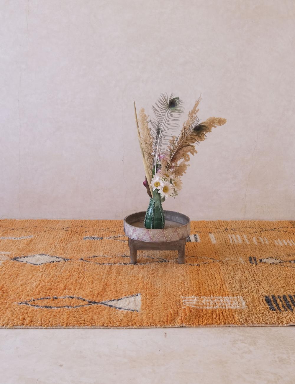 Orange patterned rug with a small table and decorative vase on a light background