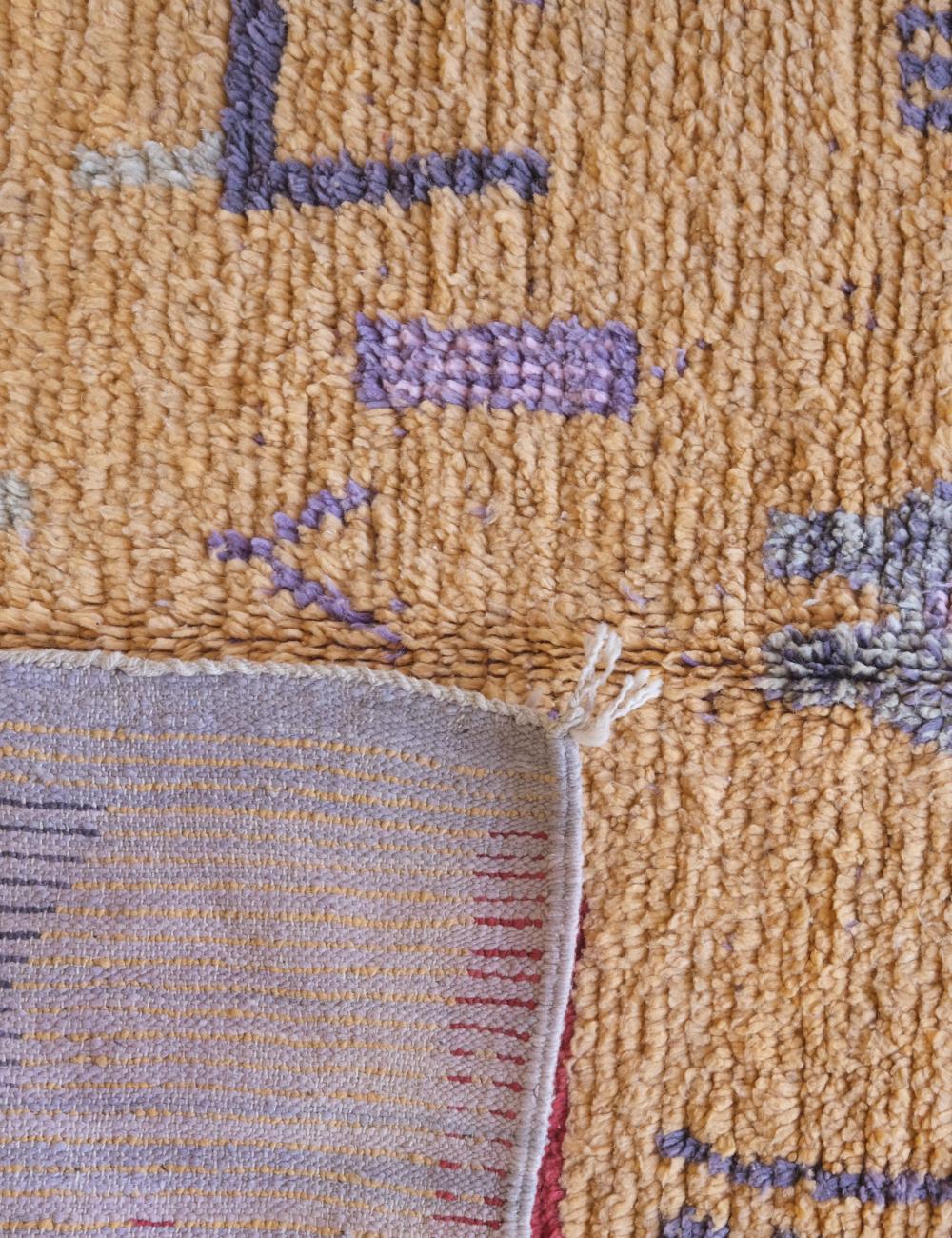 Close-up of a textured rug with geometric patterns in purple and beige.