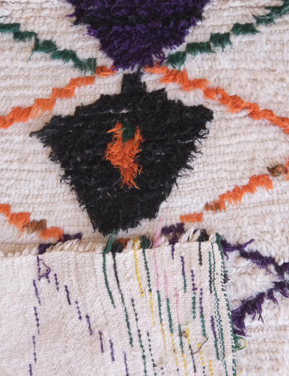 Close-up of a textured fabric with geometric patterns in black, orange, purple, and green.