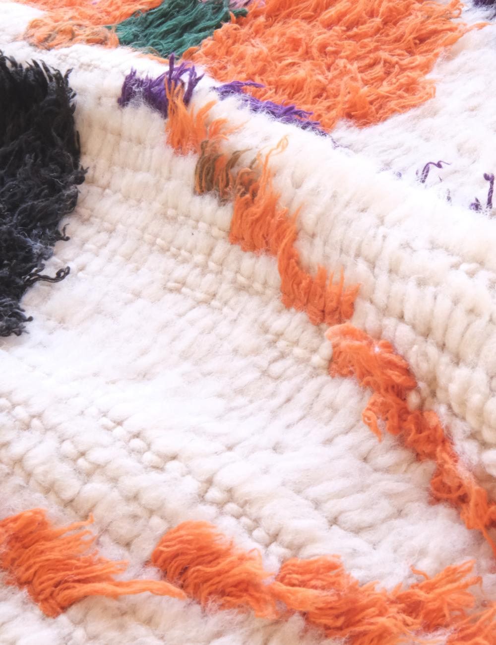Close-up of a textured rug with orange, black, and purple patterns on a white background