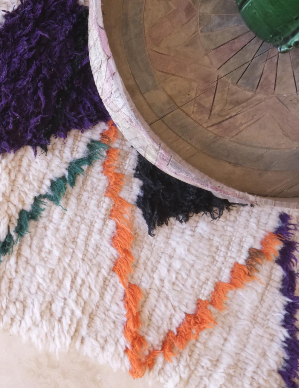 Close-up of a textured rug with geometric patterns and a wooden table corner.