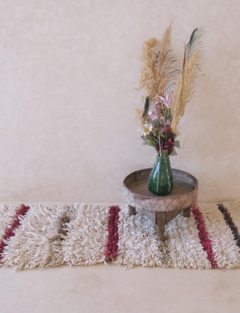 Small round wooden table with a vase of flowers and dried plants on a textured rug.