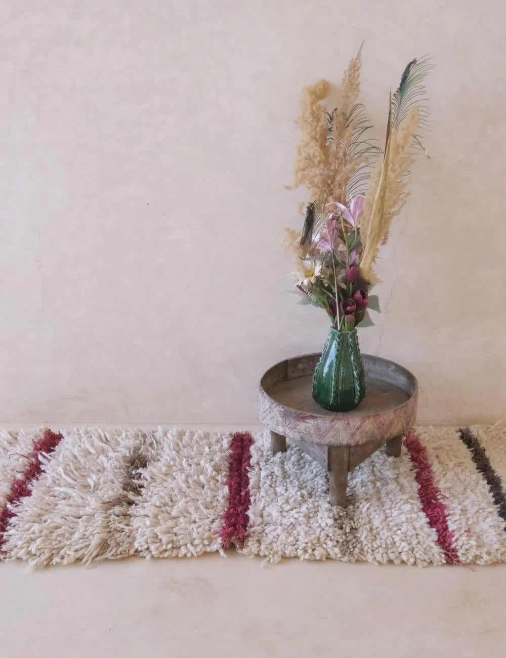 Small round wooden table with a vase of flowers and dried plants on a textured rug.