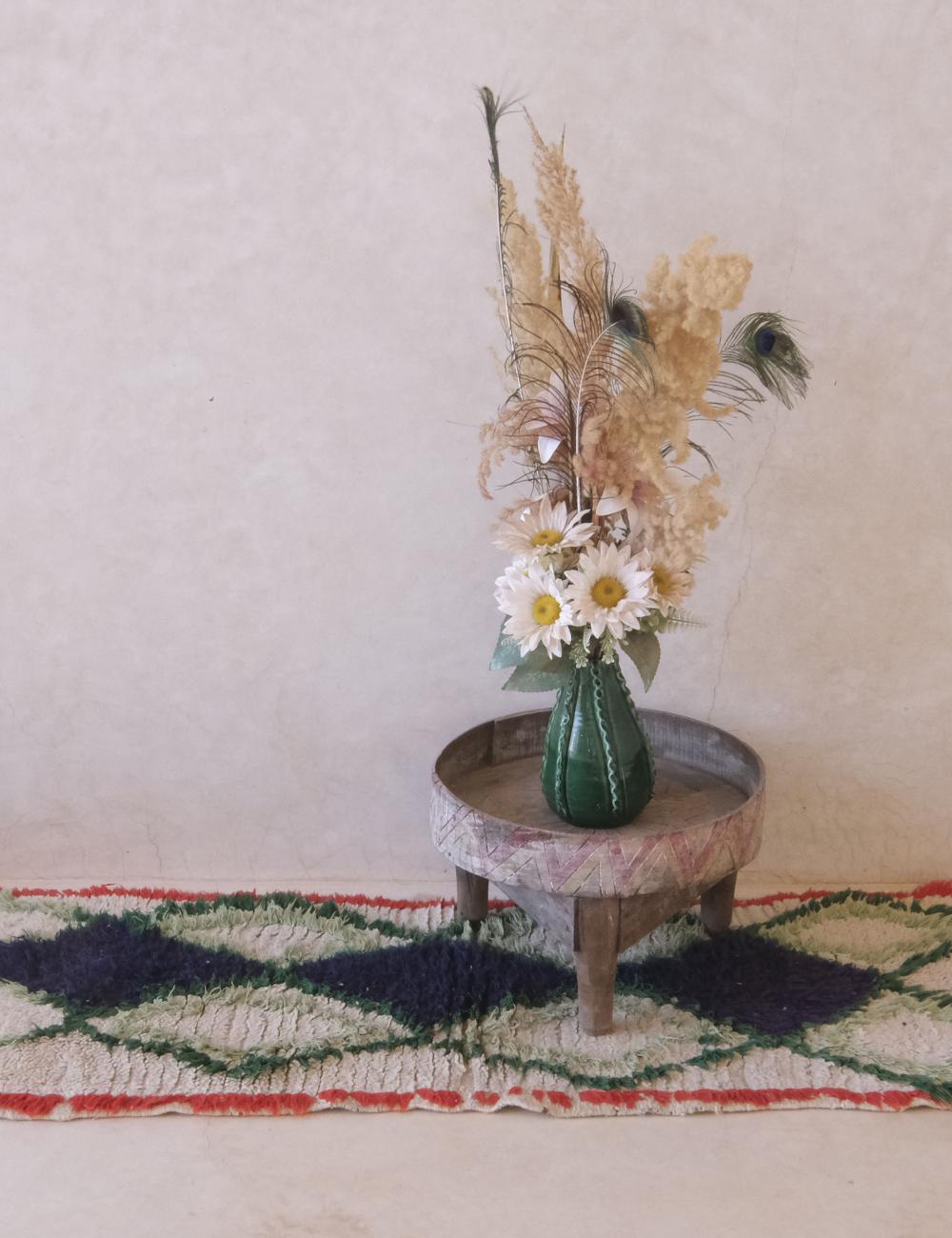Decorative vase with flowers on a small table against a plain wall.
