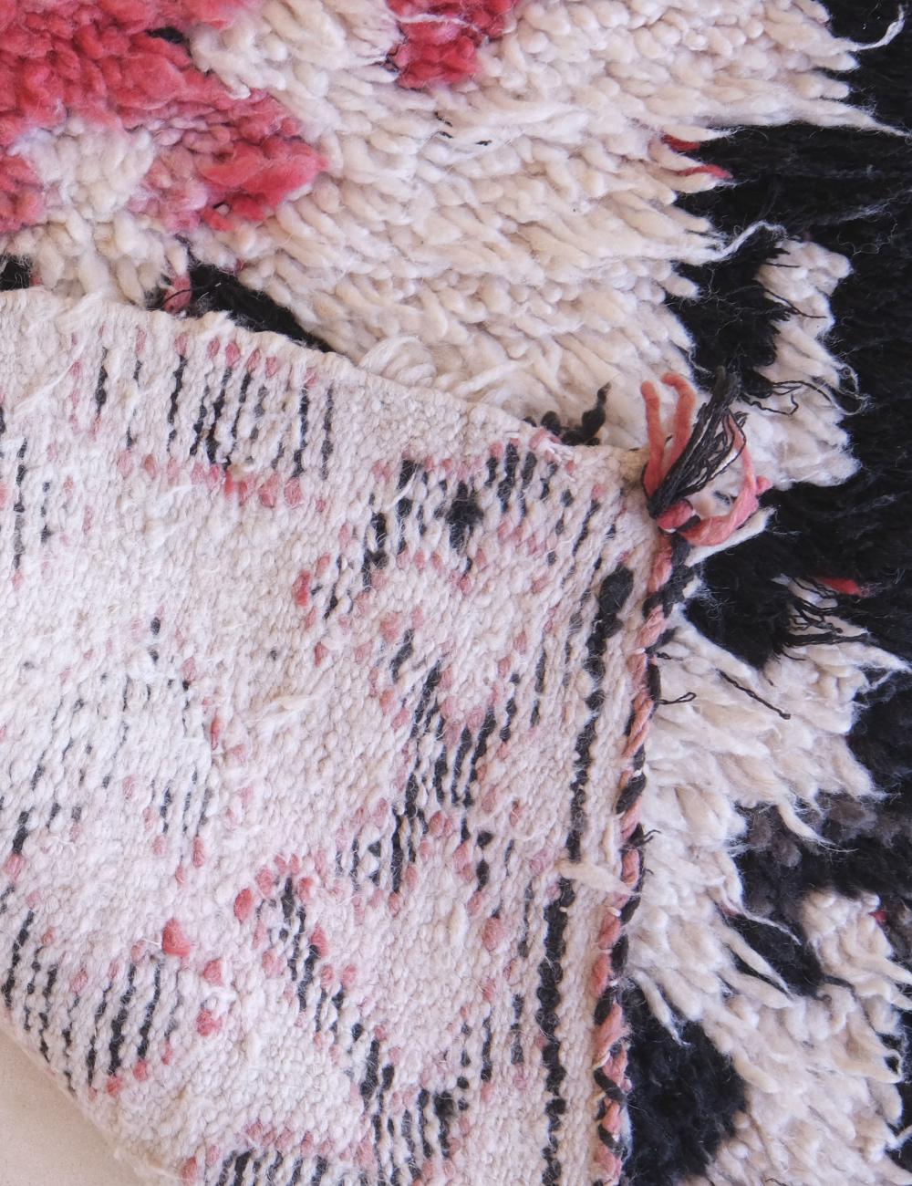 Close-up of a textured rug with pink, black, and white patterns.