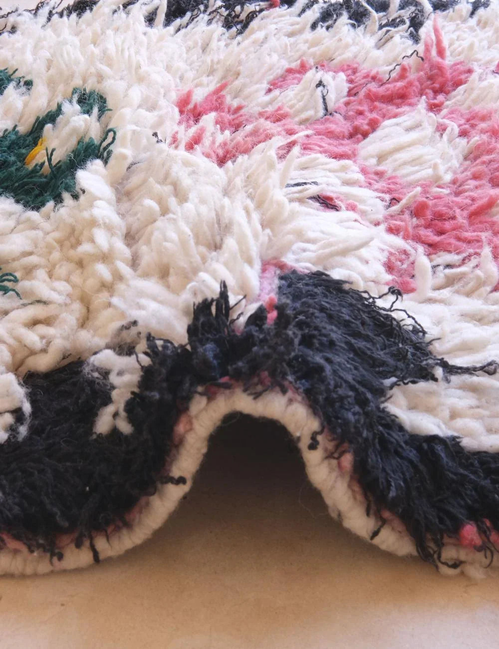 Close-up of a textured fabric with black, pink, and green patterns on a beige surface.