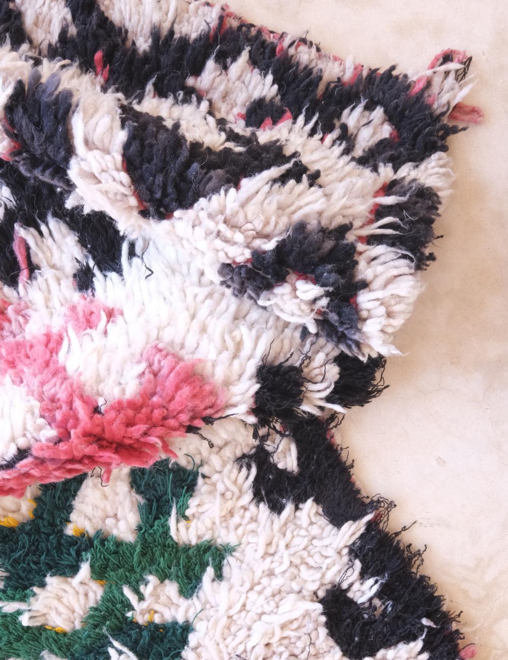 Close-up of a textured rug with black, pink, and green patterns on a beige background