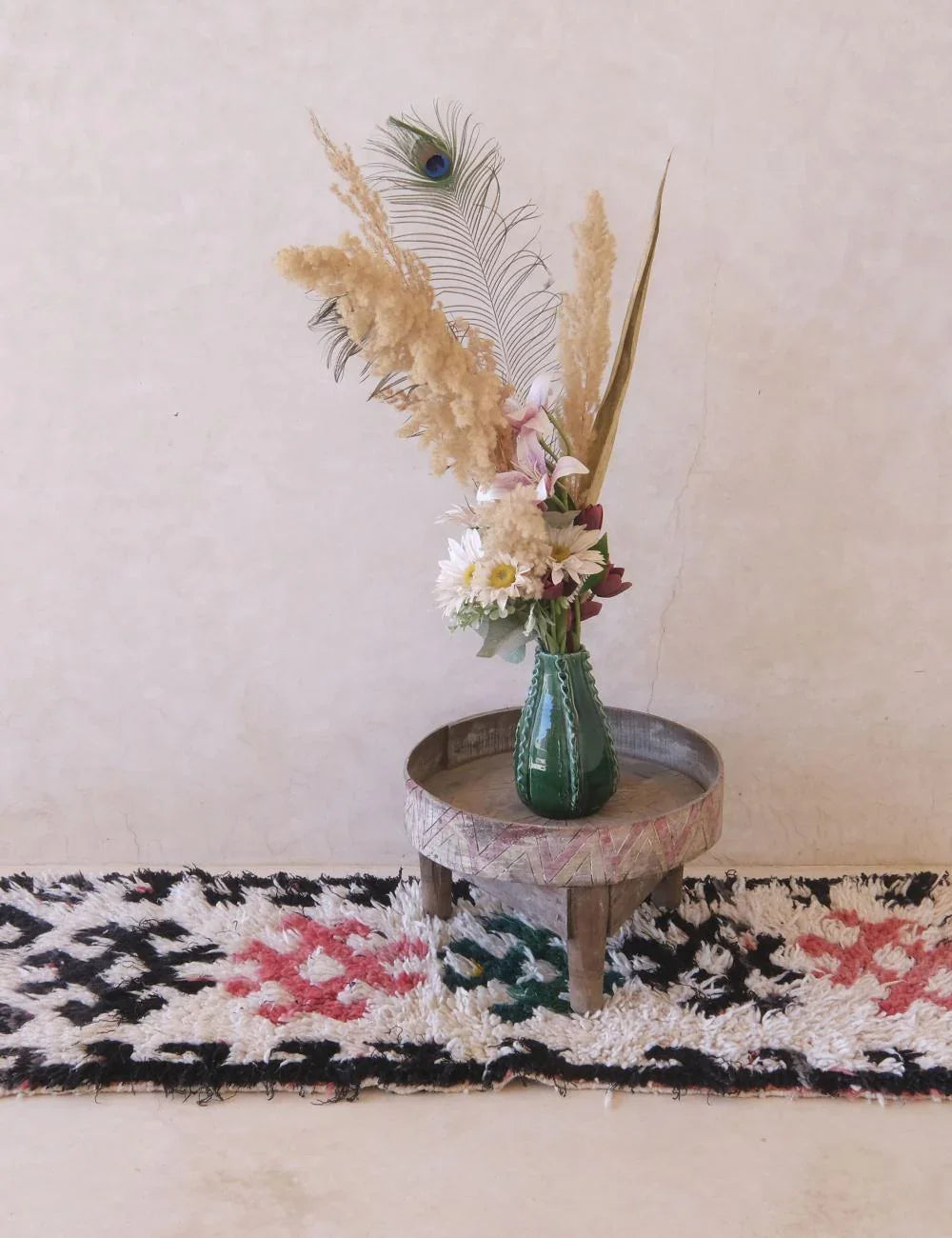 Decorative vase with flowers and peacock feathers on a small round table against a plain wall.