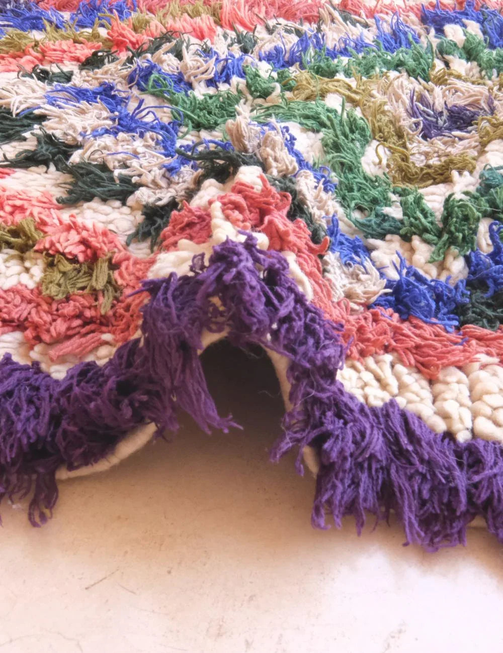 Multicolored textured rug with a purple fringe on a light background