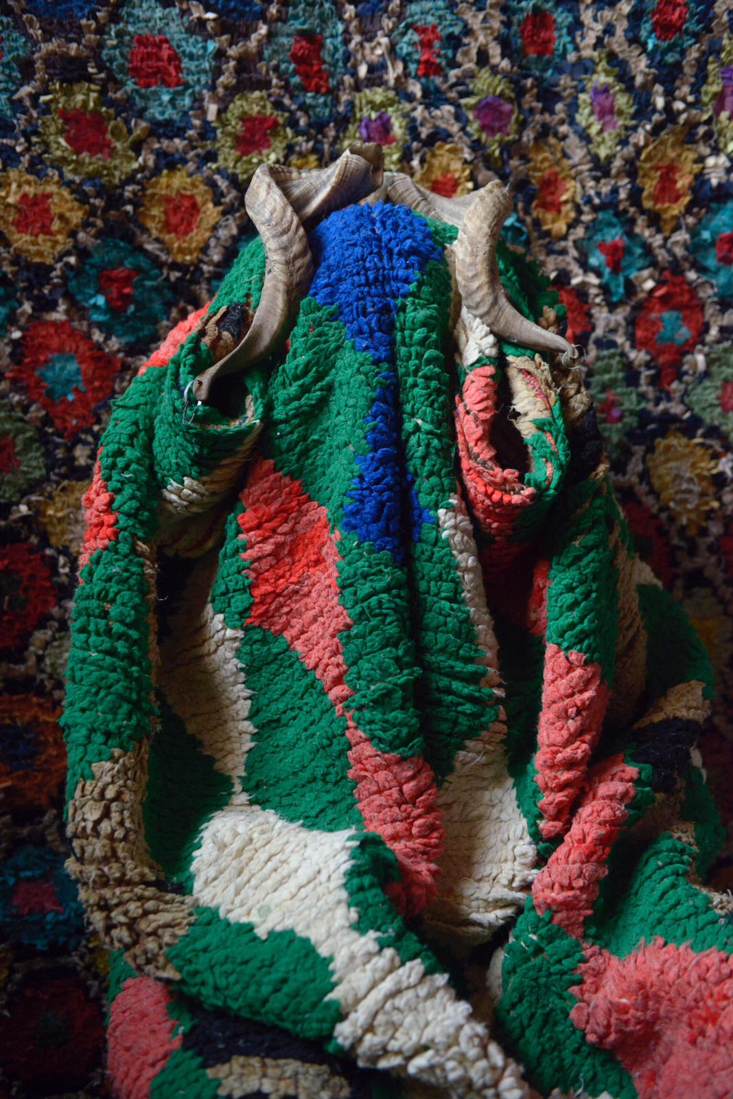 Horned mask wrapped in thick green, coral and ivory vintage rug with geometric background.