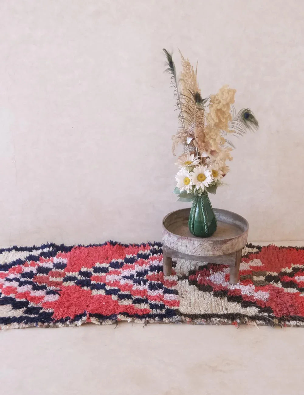 Decorative rug with geometric pattern, small table with vase and flowers against a plain wall.