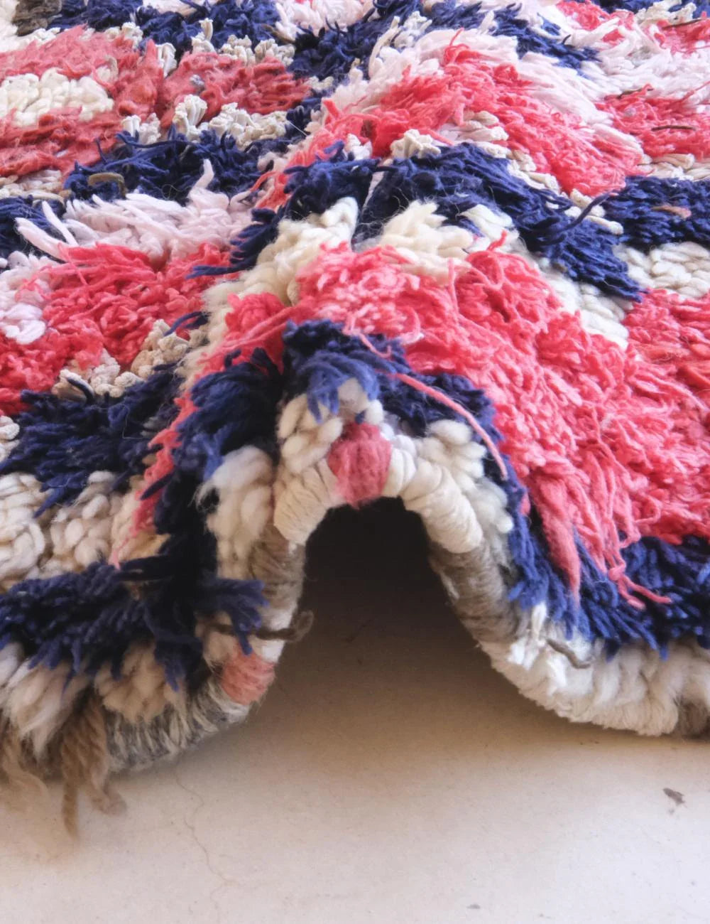 Close-up of a textured rug with pink, blue, and beige pattern on a light background