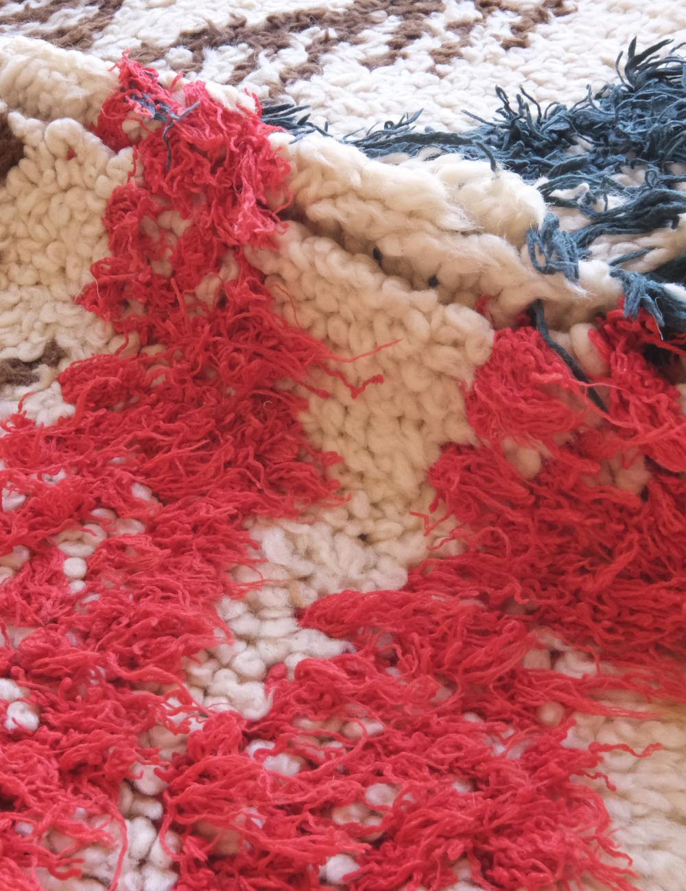 Close-up of a textured fabric with red, beige, and blue yarn.