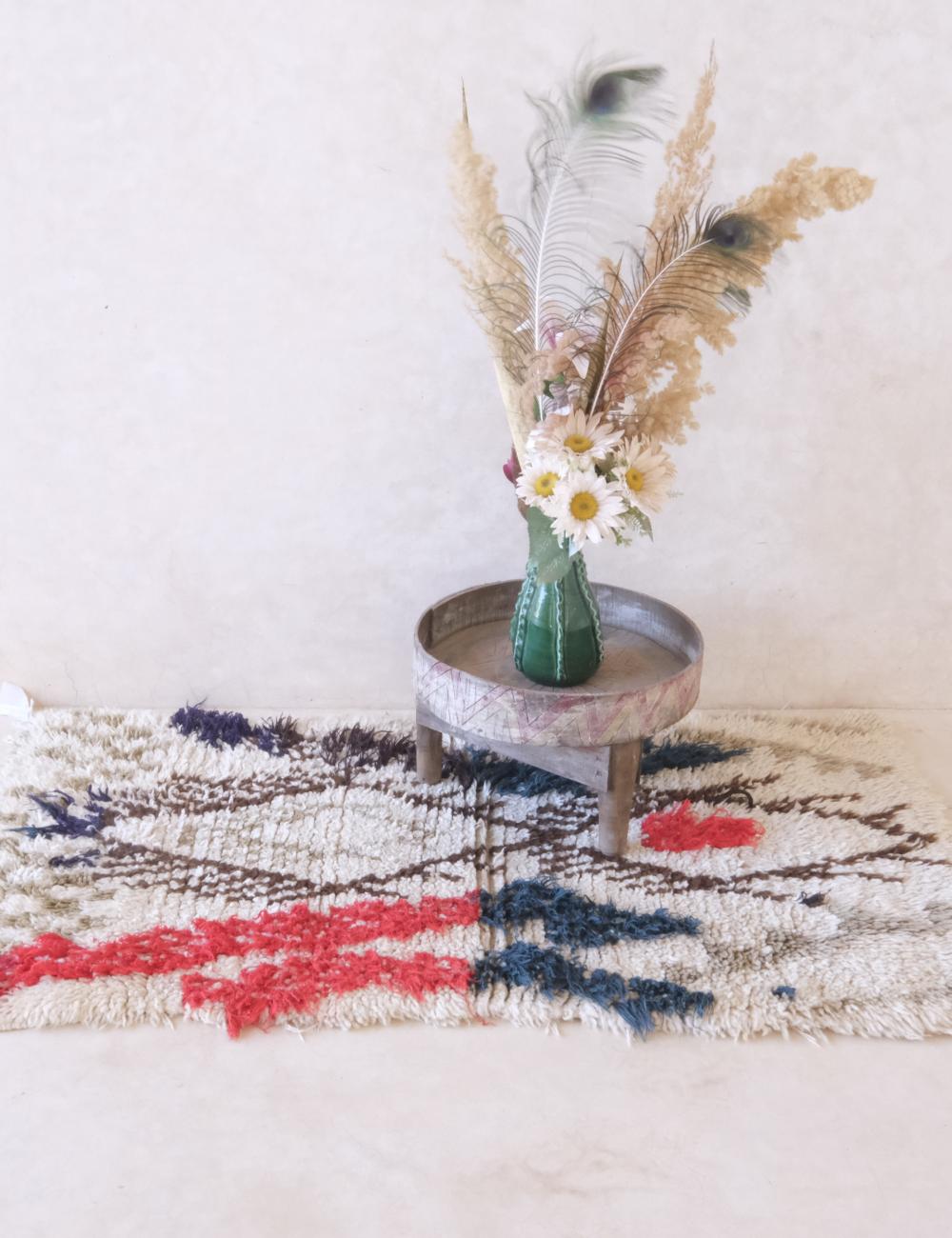 Small round table with a vase of flowers and feathers on a textured rug